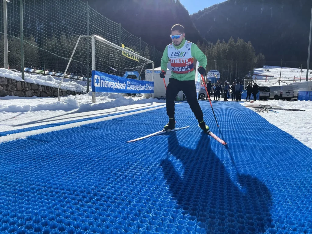 图中展示一名专业越野滑雪运动员在 Neveplast X-Country 人造雪道上滑行训练。该技术让运动员无论天气如何都能保持高质量训练。