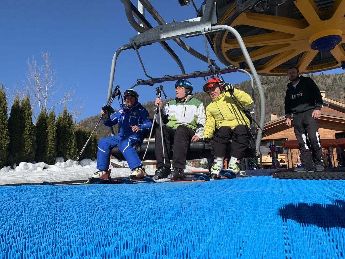 画面展示了成人滑雪者在缆车下客区的 Neveplast LIFT 表面上调整姿势，LIFT 的高耐用结构非常适合高频次使用的专业雪场。