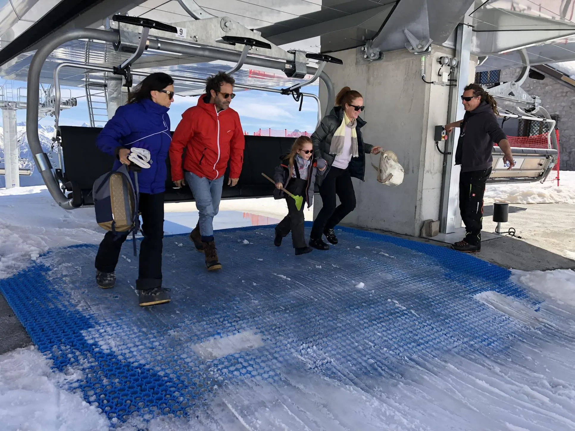 图片展示了游客家庭从缆车下客区踏上 Neveplast LIFT 人造铺面。该系统在高频使用区域保持良好抓地力与耐久性，是缆车运营者减少雪面维护成本的最佳解决方案。