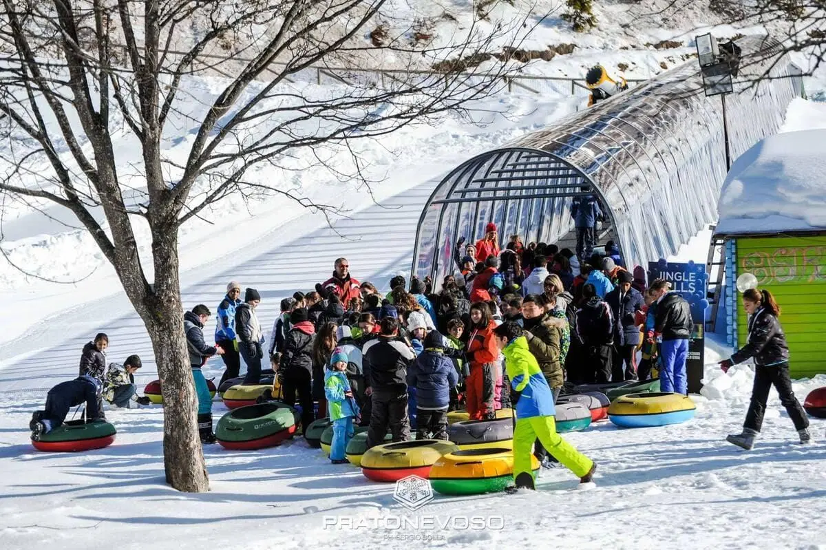 图片展示一家人在雪地上使用多彩的 SNOW TUBES 雪圈滑行。雪圈采用耐用塑料底部与高强度布料，可全年在 TUBBY 赛道或天然雪道使用。